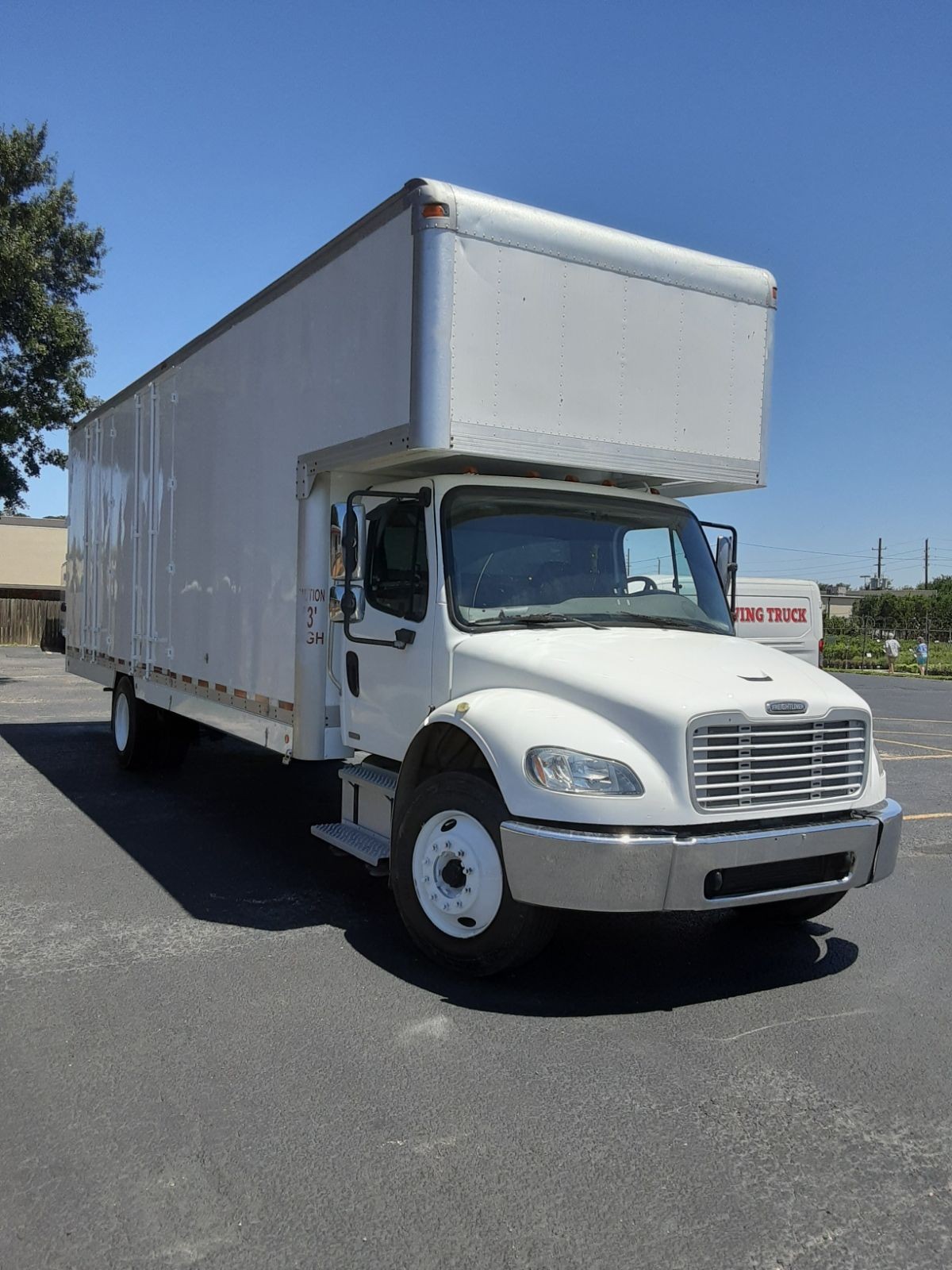 Large white delivery truck parked in a sunny parking lot with a clear blue sky in the background.