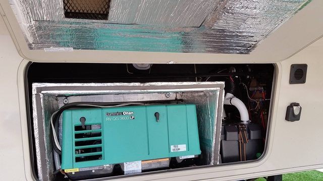 Interior view of an RV compartment containing a mounted turquoise generator, insulated with reflective material.