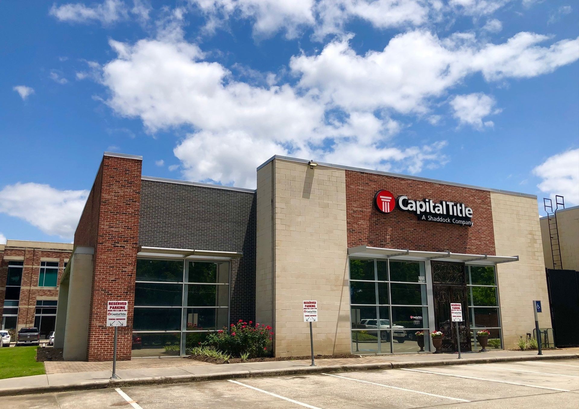 Exterior view of the Capital Title office building on a sunny day with reserved parking signs in front.